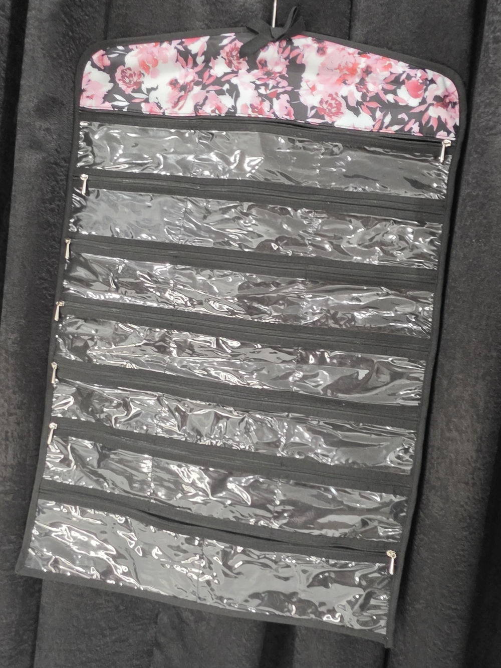 hanging floral-patterned jewelry organizer with clear zipper pockets.